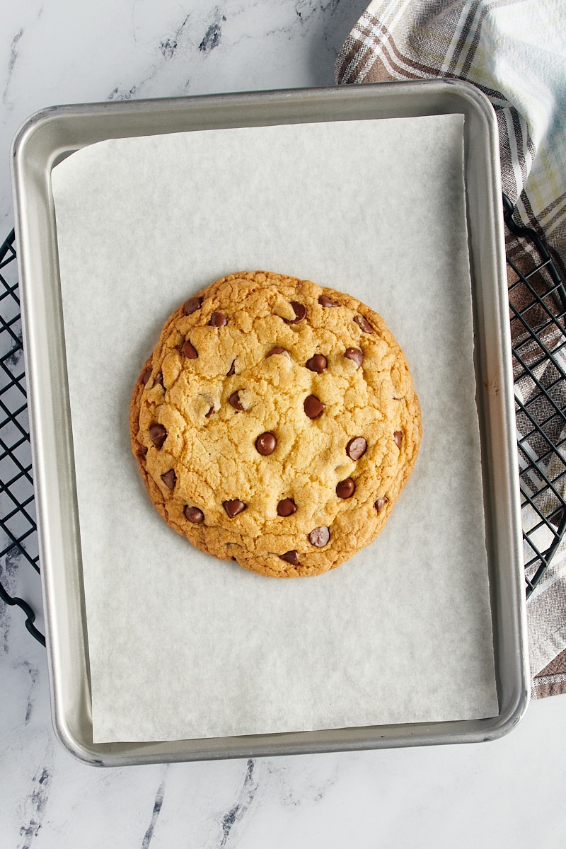 overhead view of a freshly baked giant chocolate chip cookie on a parchment-lined sheet pan