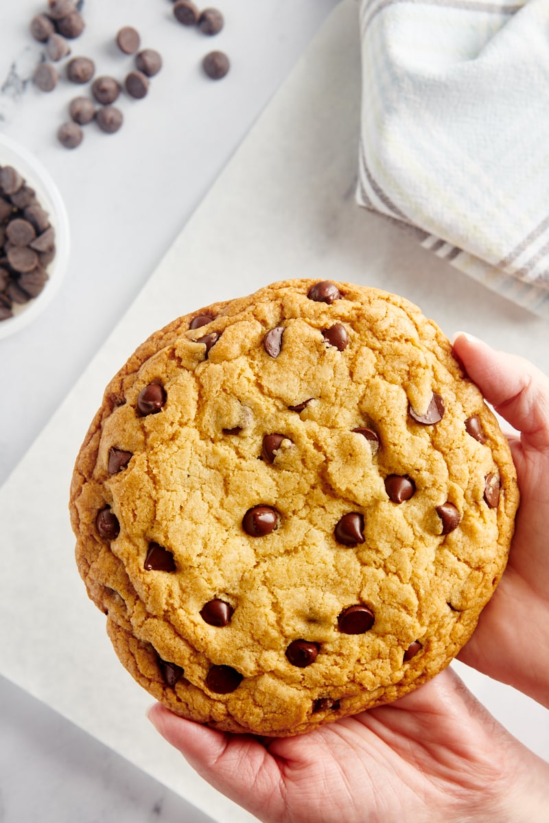 overhead view of two hands holding a giant chocolate chip cookie
