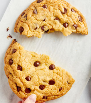 a hand reaching in to grab half of a giant chocolate chip cookie