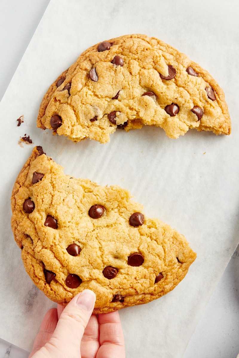 a hand reaching in to grab half of a giant chocolate chip cookie