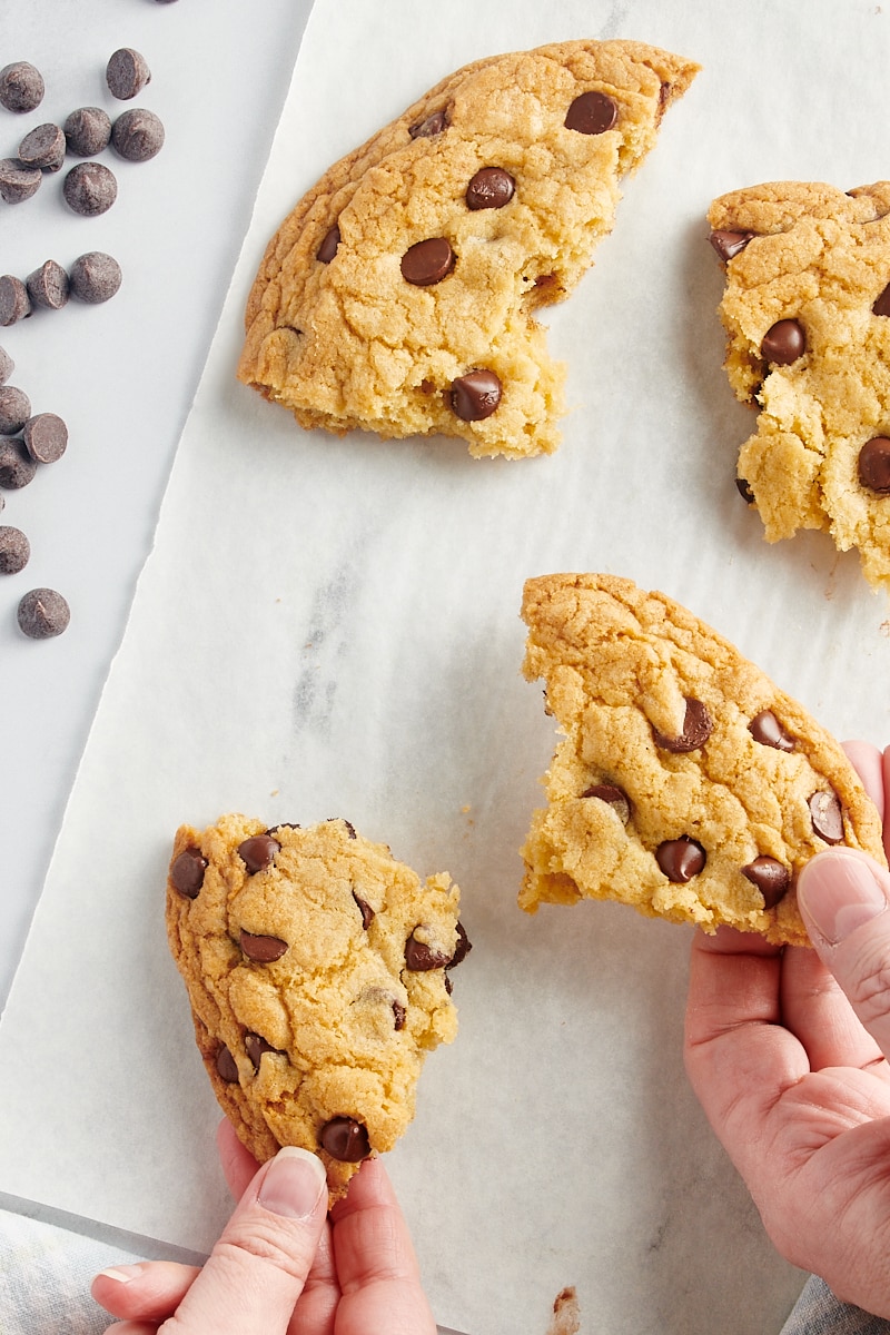 overhead view of two hands reaching for pieces of a giant chocolate chip cookie