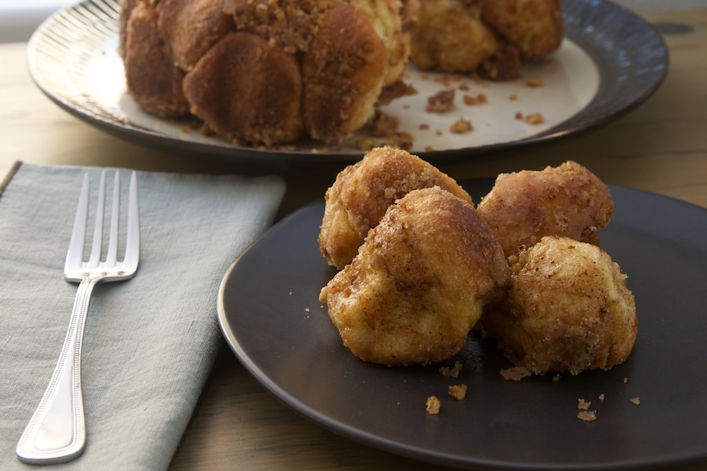 four pieces of brown butter cinnamon pull apart bread on a dark gray plate with more bread in the background