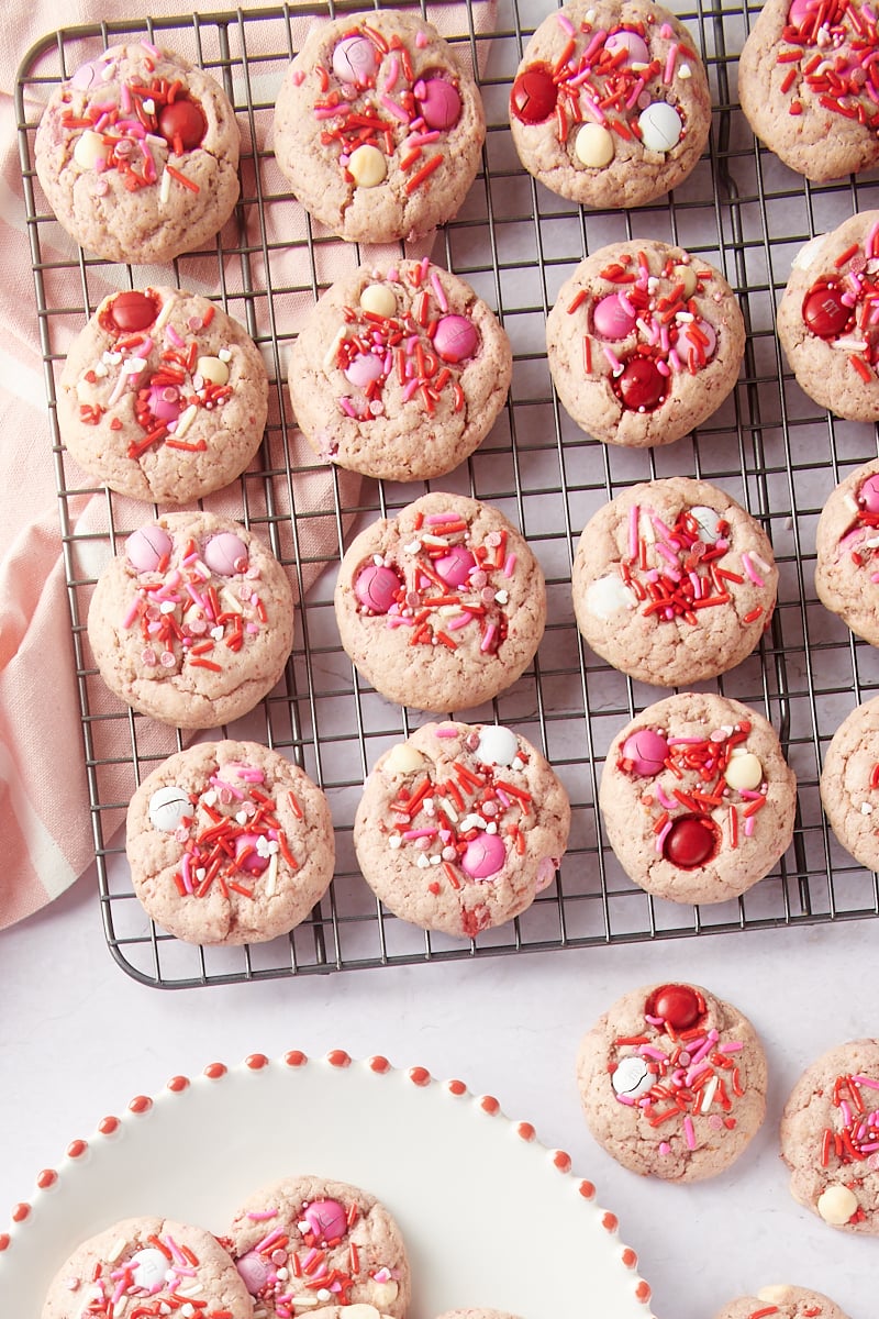 Strawberry M&M Cookies on a wire rack and on a white place and marble surface