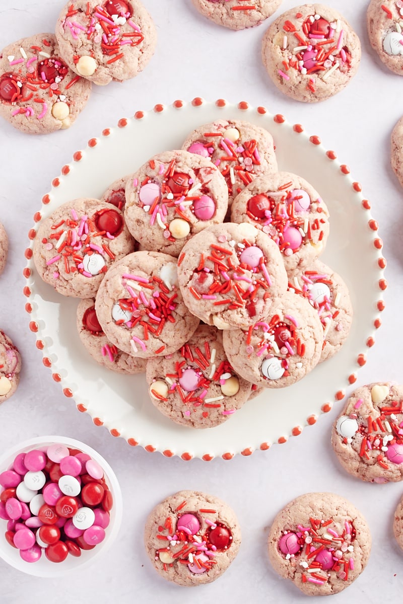 overhead view of Strawberry M&M Cookies on a red-rimmed white plate with more cookies around the plate