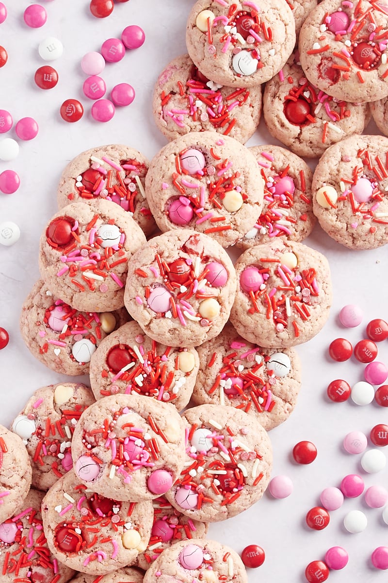 overhead view of Strawberry M&M Cookies on a marble surface with red, pink, and white M&Ms scattered around the cookies