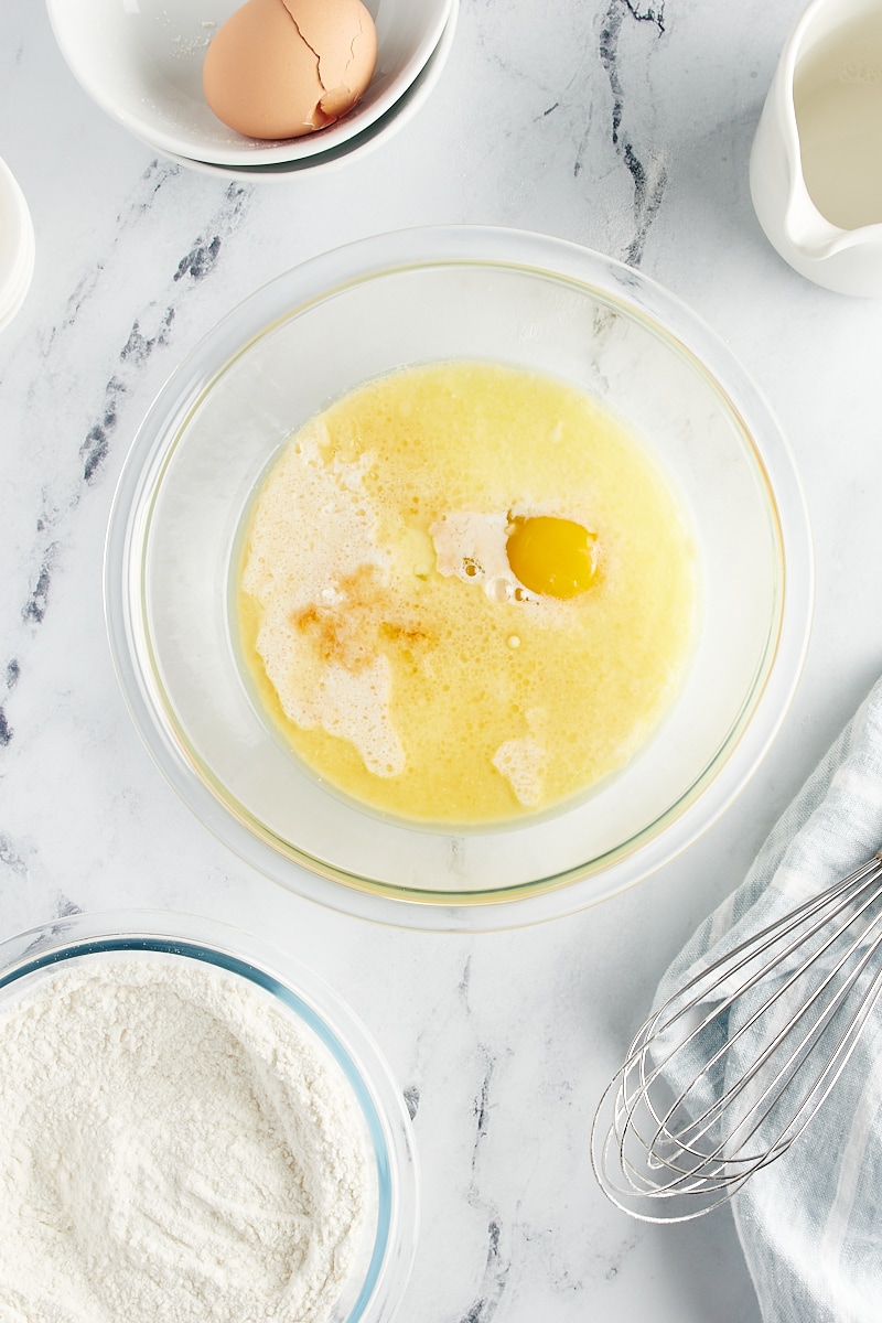 overhead view of egg, milk, melted butter, and vanilla extract in a glass mixing bowl