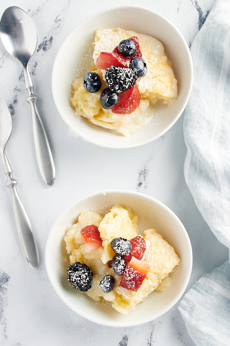 overhead view of two servings of Vanilla Pudding Cake topped with fresh berries and served in white bowls
