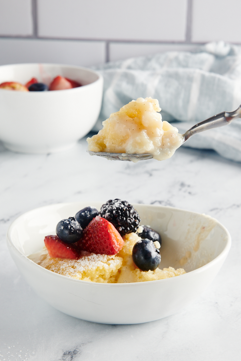 a bite of Vanilla Pudding Cake on a spoon over a bowl of cake topped with berries