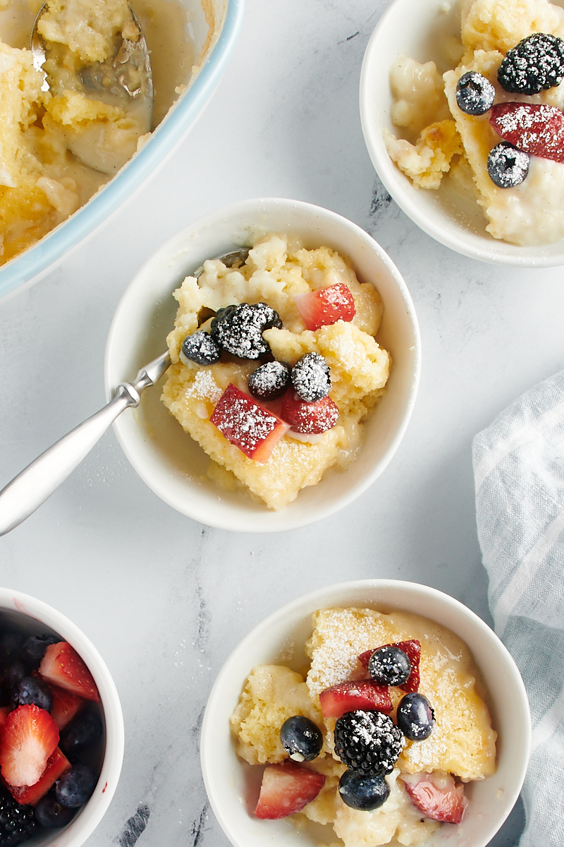 overhead view of three servings of Vanilla Pudding Cake served in white bowls and topped with fresh berries and confectioners' sugar