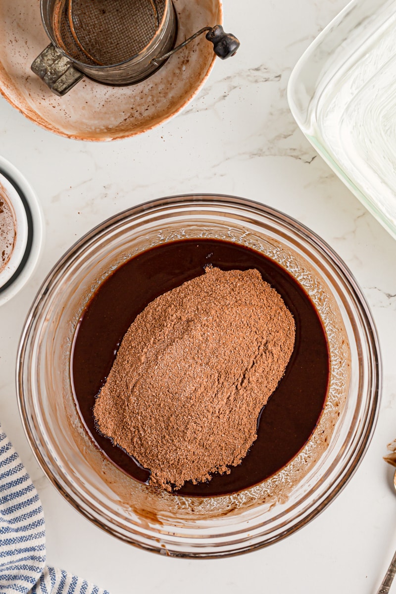 Overhead view of sugar and cocoa powder added to melted chocolate in mixing bowl
