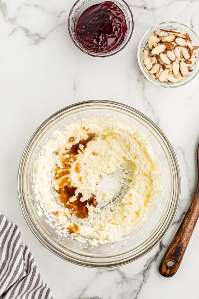 overhead view of vanilla and almond extracts added to creamed butter and sugar in a glass mixing bowl