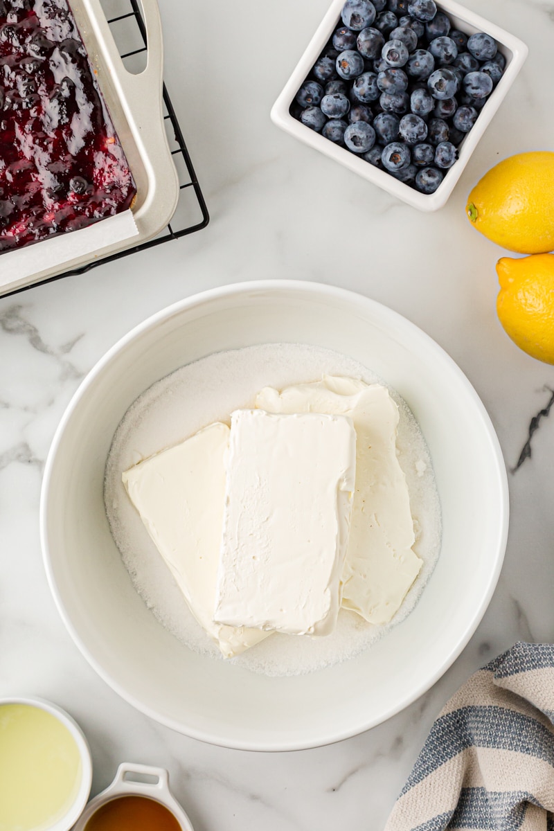 Overhead view of cream cheese bars and sugar in mixing bowl