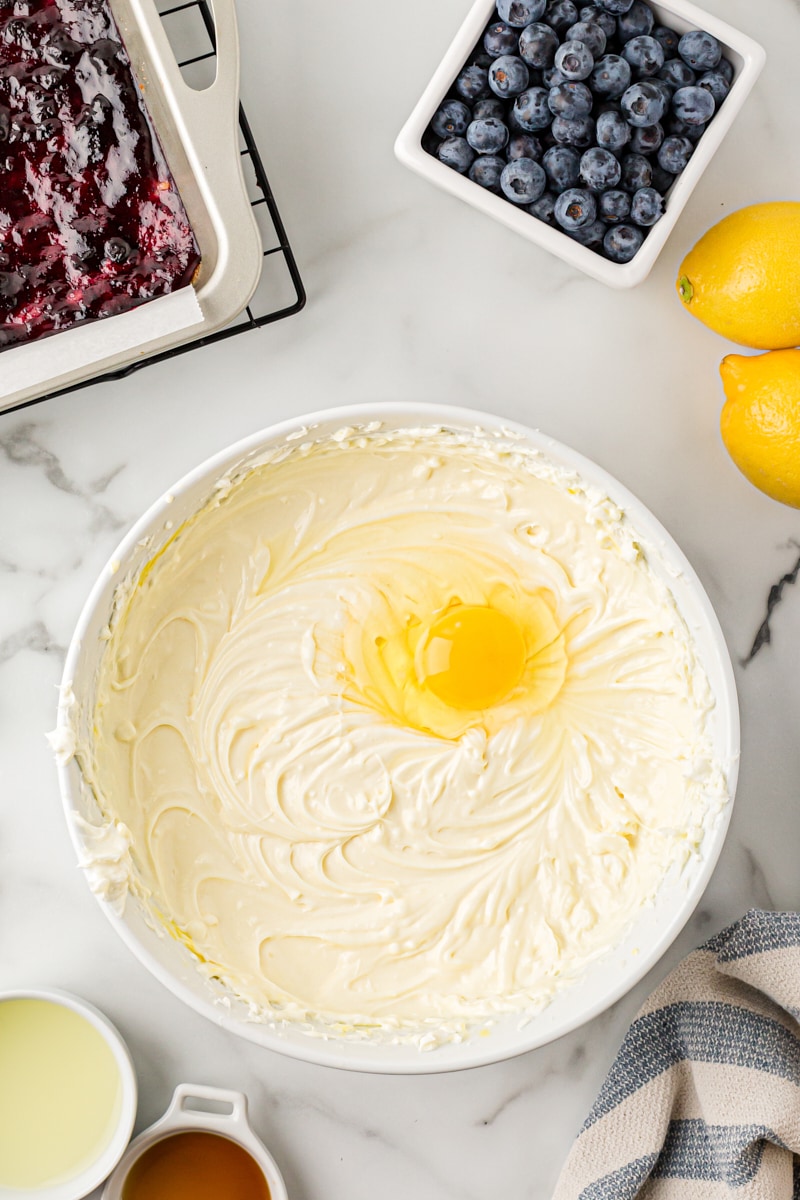 Overhead view of egg added to cheesecake batter in bowl