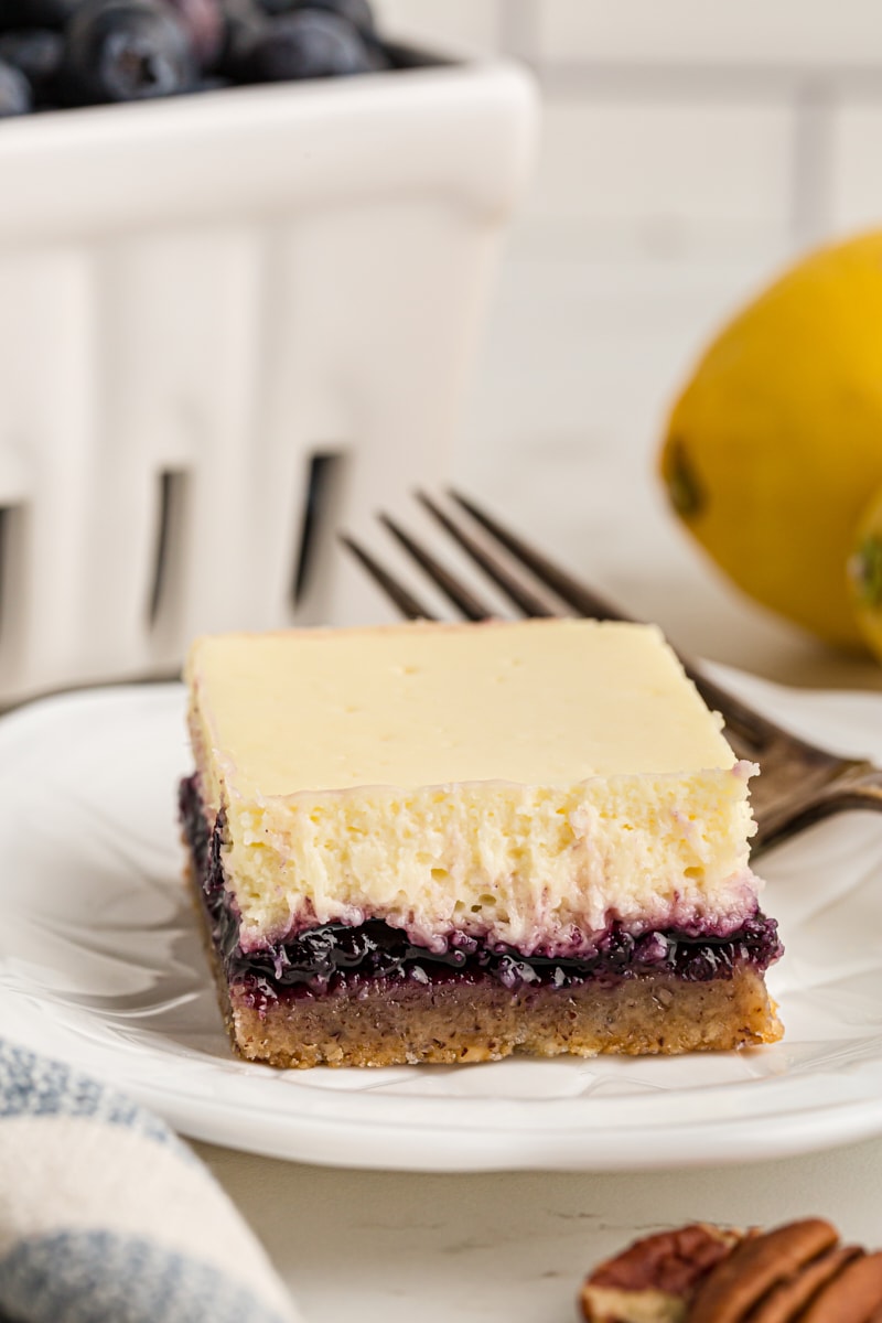 Lemon blueberry cheesecake bar on plate, with forkful removed