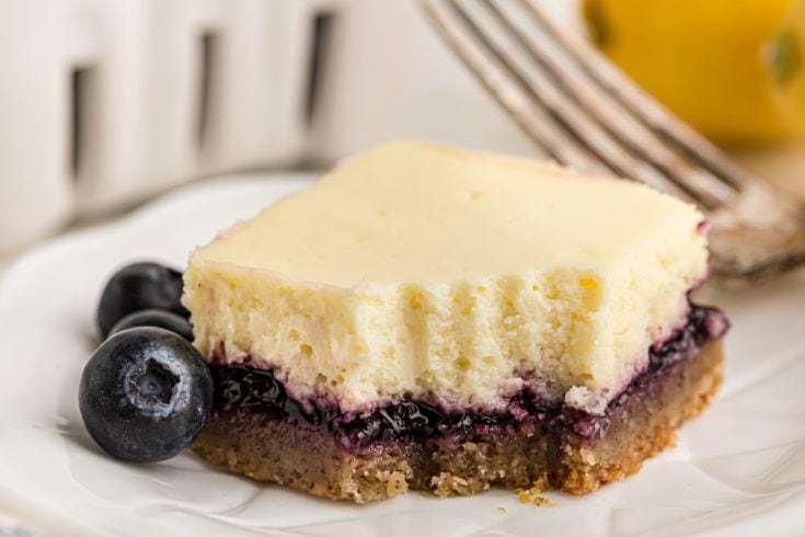 Lemon blueberry cheesecake bar on plate, with forkful removed
