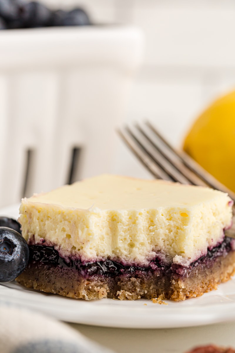 Lemon blueberry cheesecake bar on plate, with forkful removed