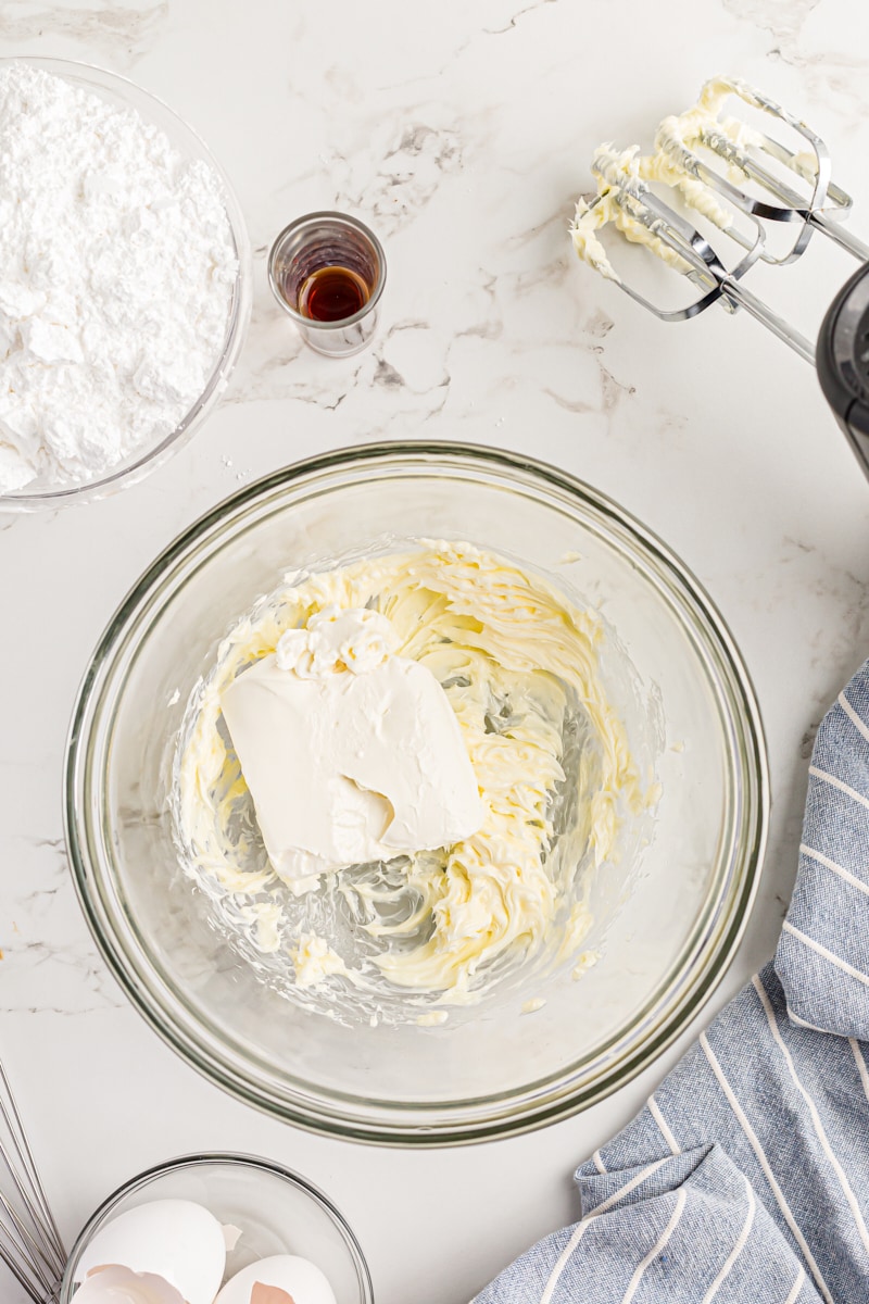 Overhead view of cream cheese block in mixing bowl of whipped butter