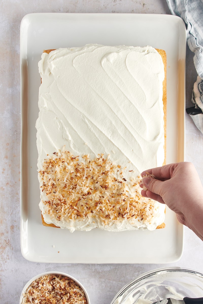 overhead view of toasted coconut being sprinkled over coconut cake