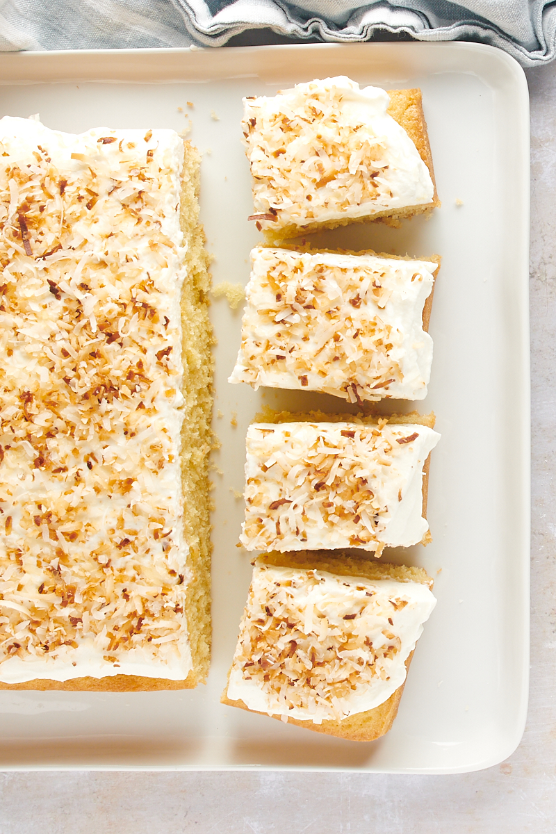 overhead view of partially sliced Coconut Sheet Cake on a white serving tray