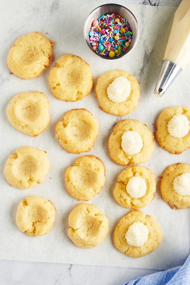 overhead view of thumbprint cookies on parchment paper; some filled with frosting