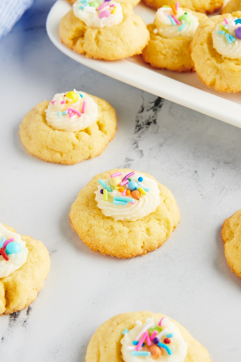 several Frosting-Filled Thumbprint Cookies on a marble surface next to a plate of more cookies