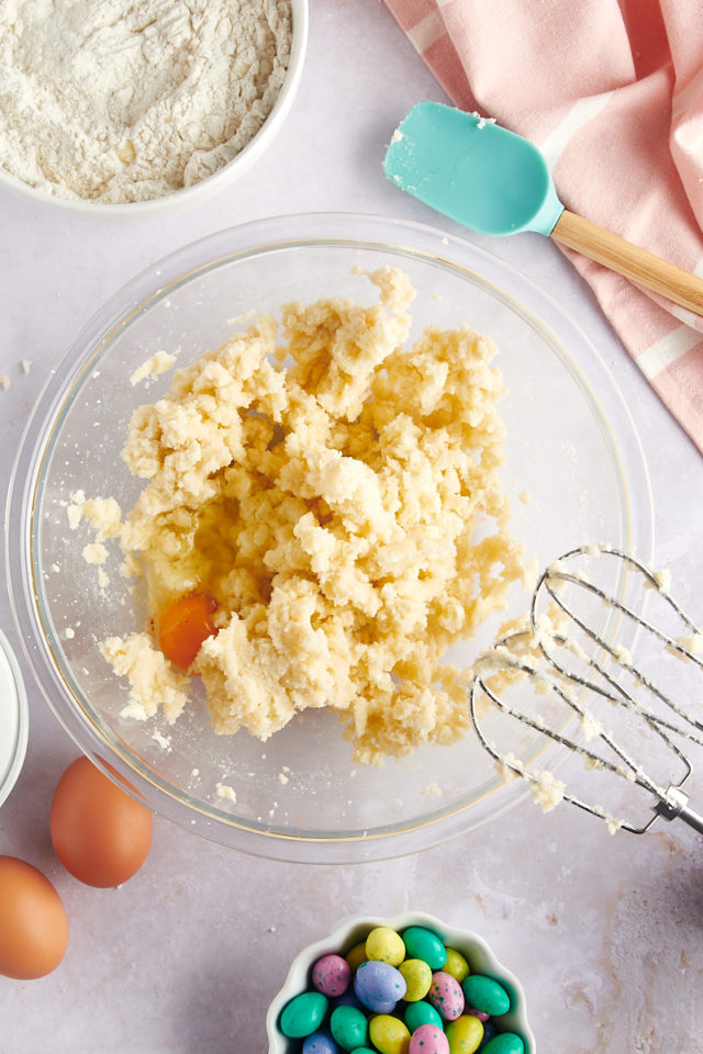 overhead view of an egg added to creamed butter and sugar in a glass mixing bowl