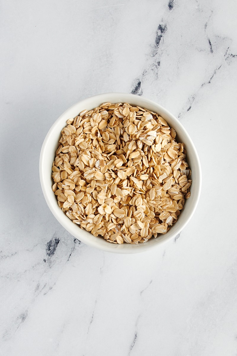 overhead view of rolled oats in a white bowl on a marble surface