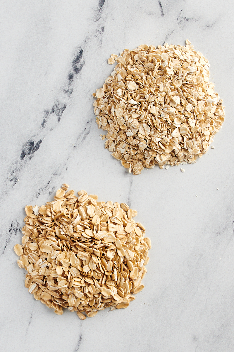 side by side piles of rolled oats and quick oats on a marble surface