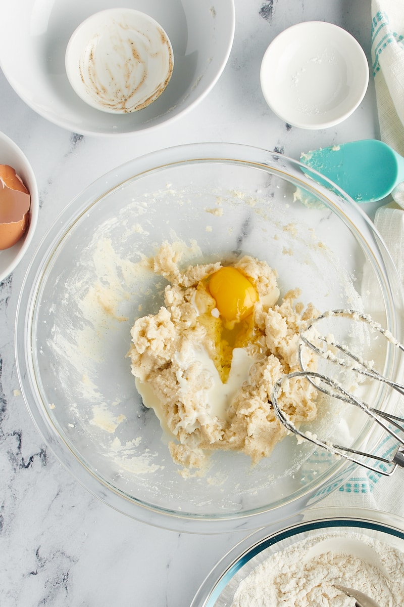 Overhead view of egg added to mixing bowl with butter and sugar