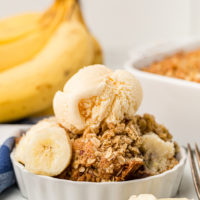 Banana bread cobbler in dish topped with banana slices and scoop of vanilla ice cream
