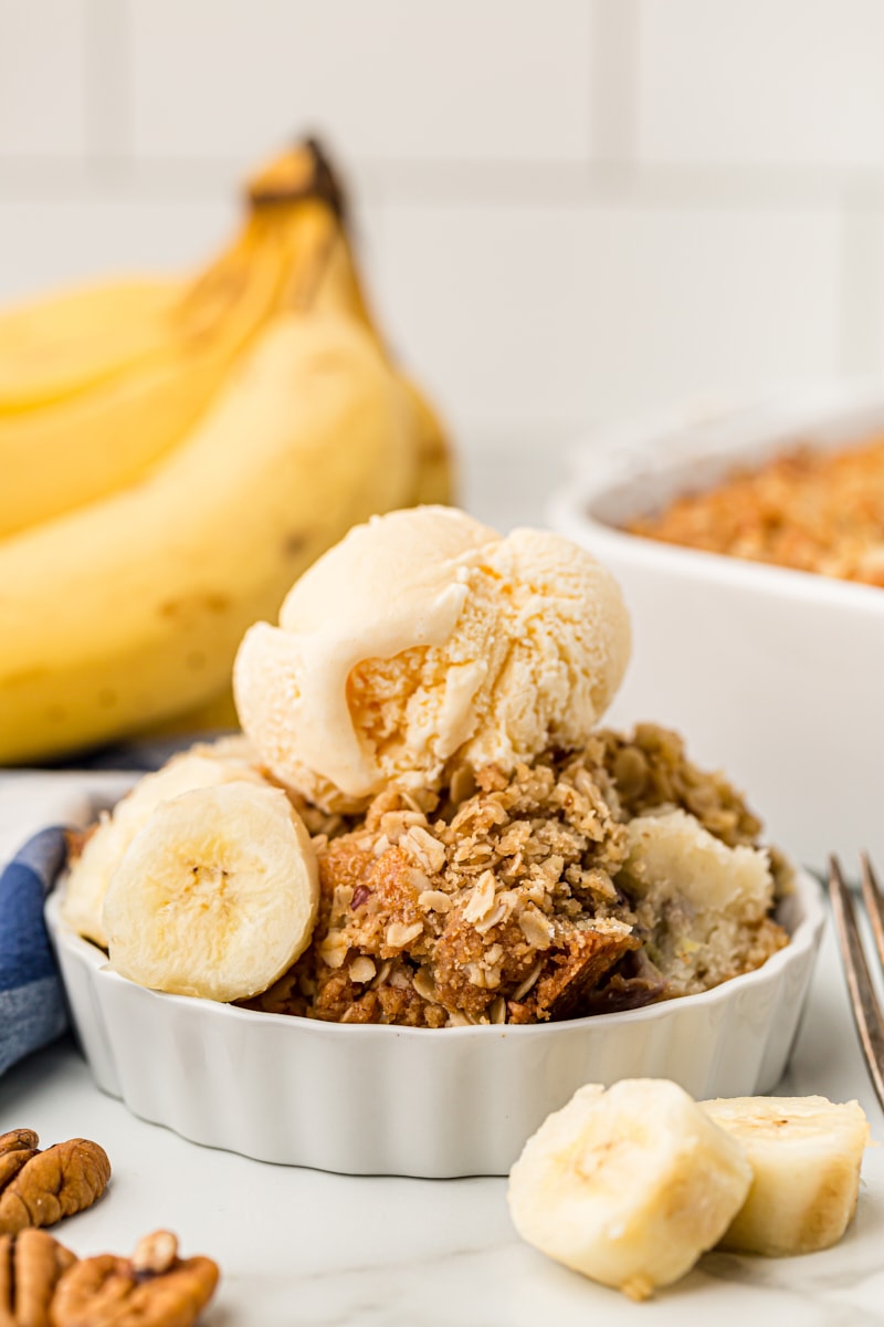 Banana bread cobbler in dish topped with banana slices and scoop of vanilla ice cream