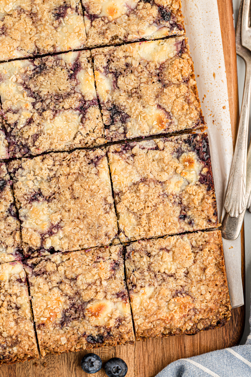 Overhead view of cut blueberry jam cream cheese bars on wood cutting board