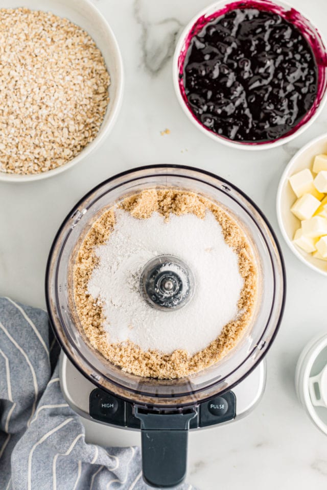 Overhead view of crust ingredients in food processor and blueberry jam in bowl