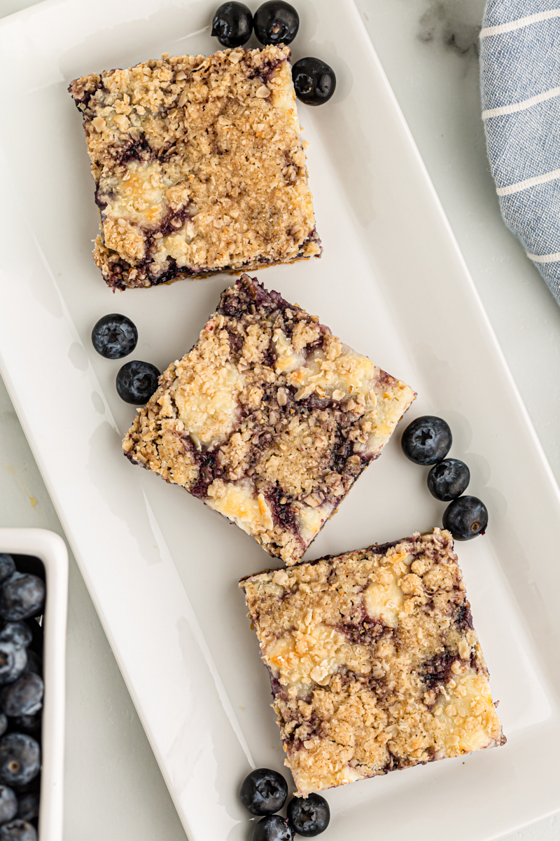 Overhead view of 3 blueberry jam cream cheese bars on serving plate with blueberries