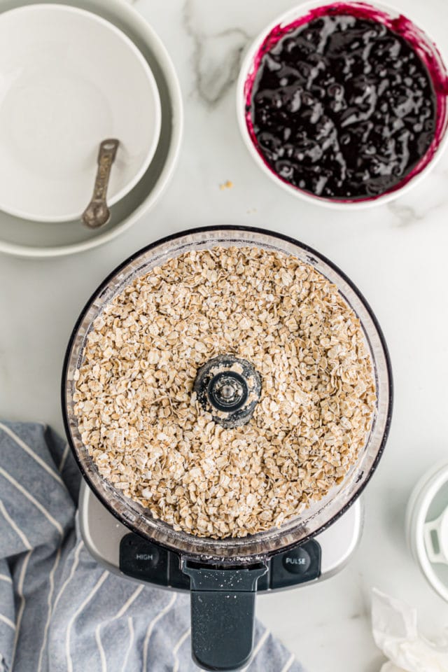 Overhead view of crust ingredients in food processor and blueberry jam in bowl