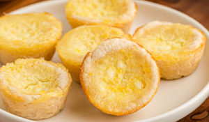 Lemon Chess Tartlets on a white plate on top of a wooden serving board