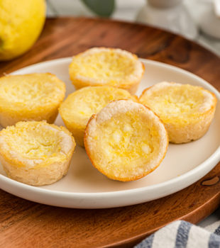 Lemon Chess Tartlets on a white plate on top of a wooden serving board