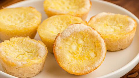 Lemon Chess Tartlets on a white plate on top of a wooden serving board