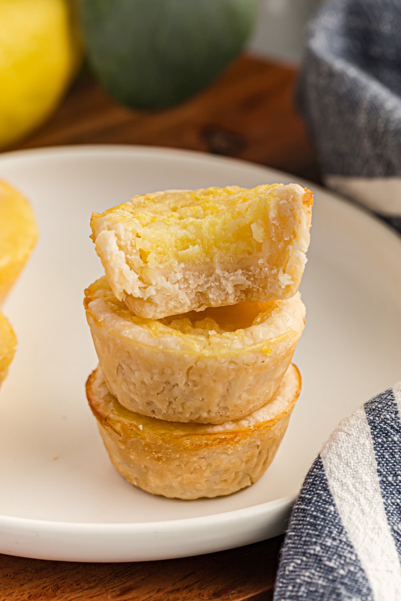 half of a Lemon Chess Tartlet stacked on top of two more tartlets on a white plate