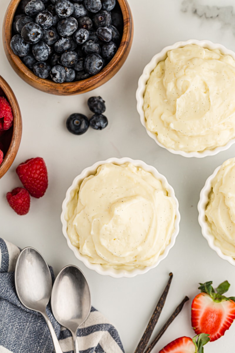 Overhead view of vanilla pudding in 3 custard cups and fresh berries