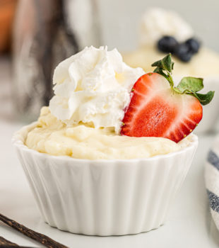 Cup of vanilla pudding topped with whipped cream and halved strawberry