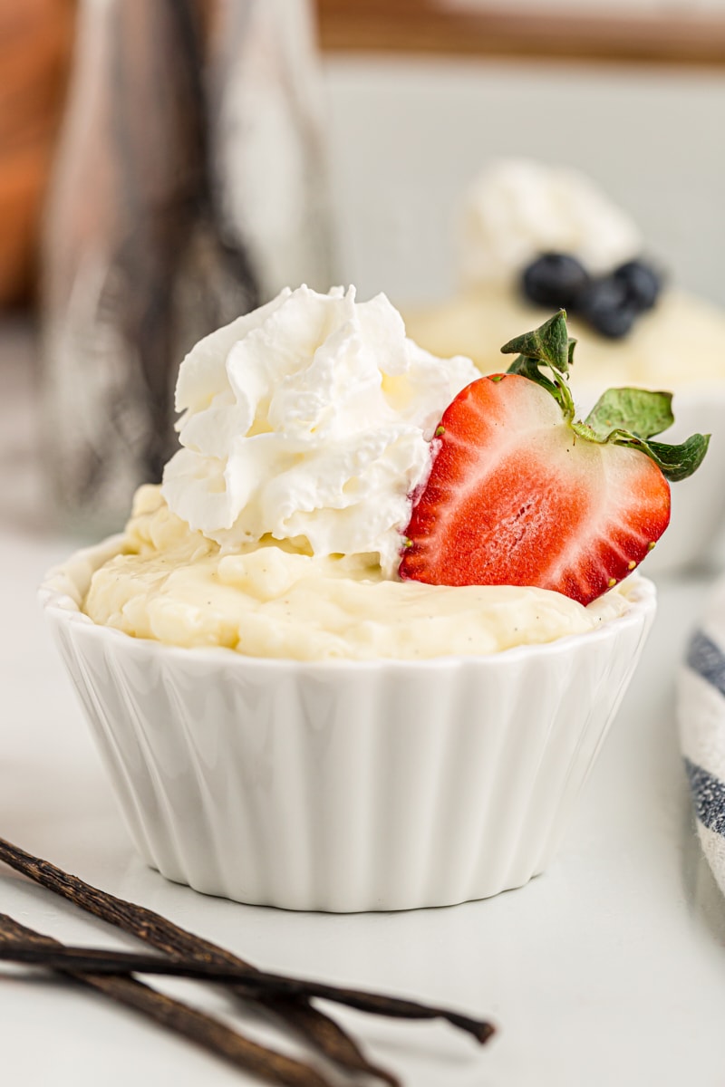 Cup of vanilla pudding topped with whipped cream and halved strawberry