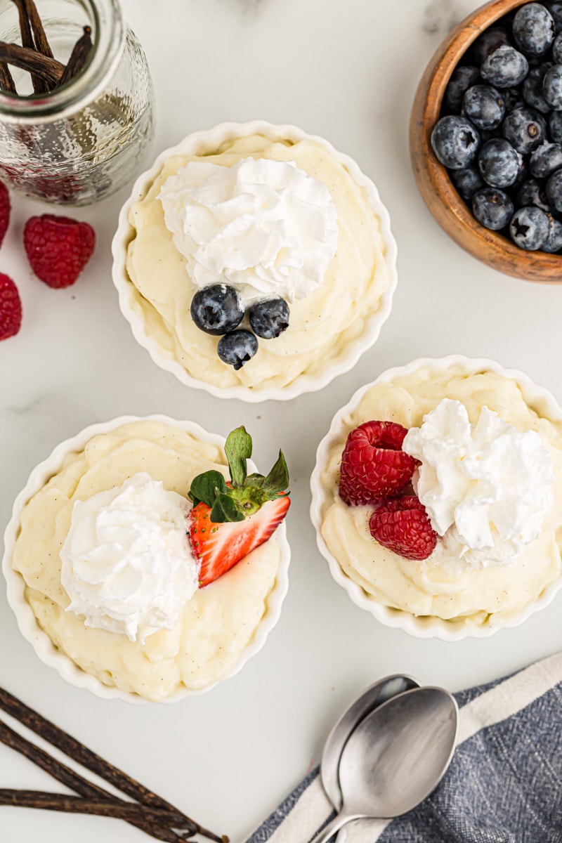 Overhead view of 3 cups of vanilla pudding topped with whipped cream and berries