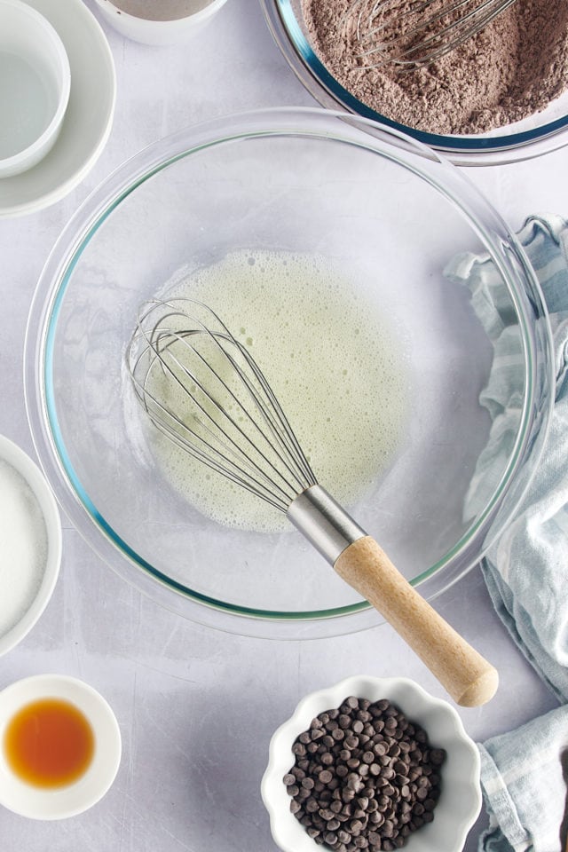 Overhead view of foamy egg whites in mixing bowl with whisk