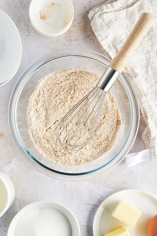 Overhead view of dry muffin ingredients in glass mixing bowl with whisk