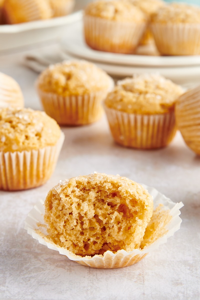 Half-eaten cinnamon mini muffin set on muffin wrapper, with additional muffins in background