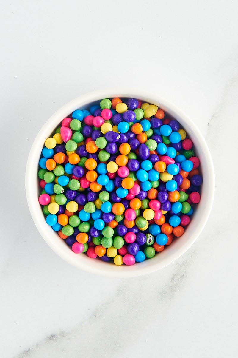 overhead view of rainbow sixlets in a white bowl on a marble surface