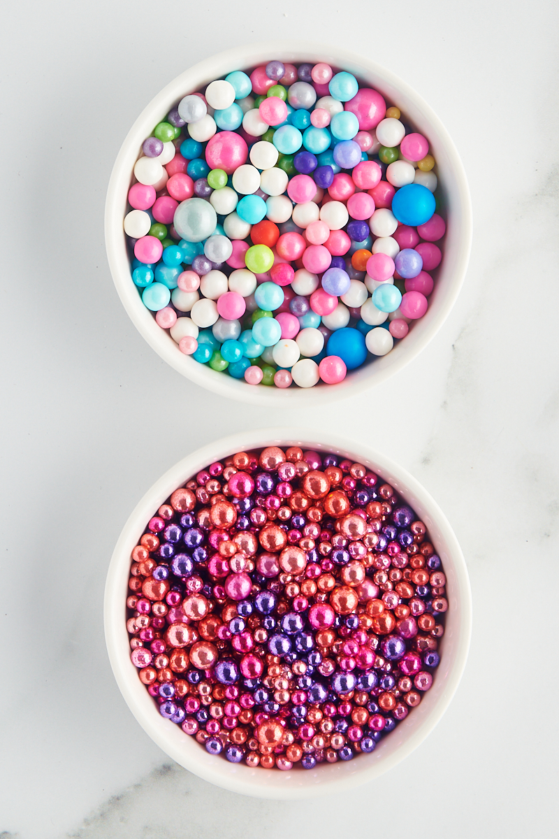 overhead view of dragées and sugar pearls in white bowls on a marble surface