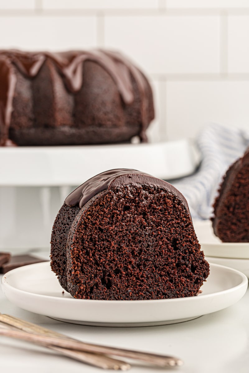Slice of chocolate sour cream Bundt cake on plate, with whole cake in background on stand