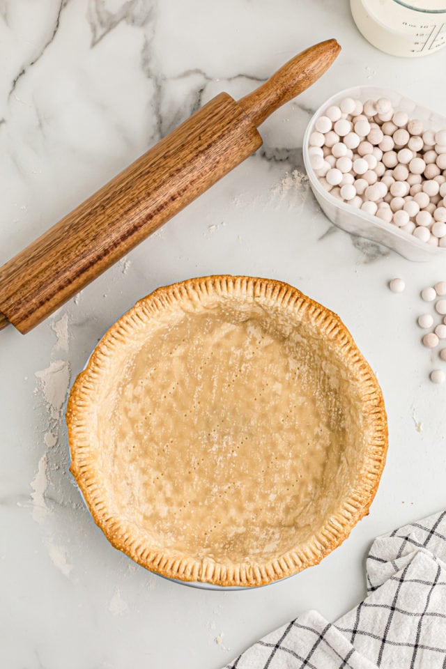 Overhead view of pie crust next to rolling pin and pie weights